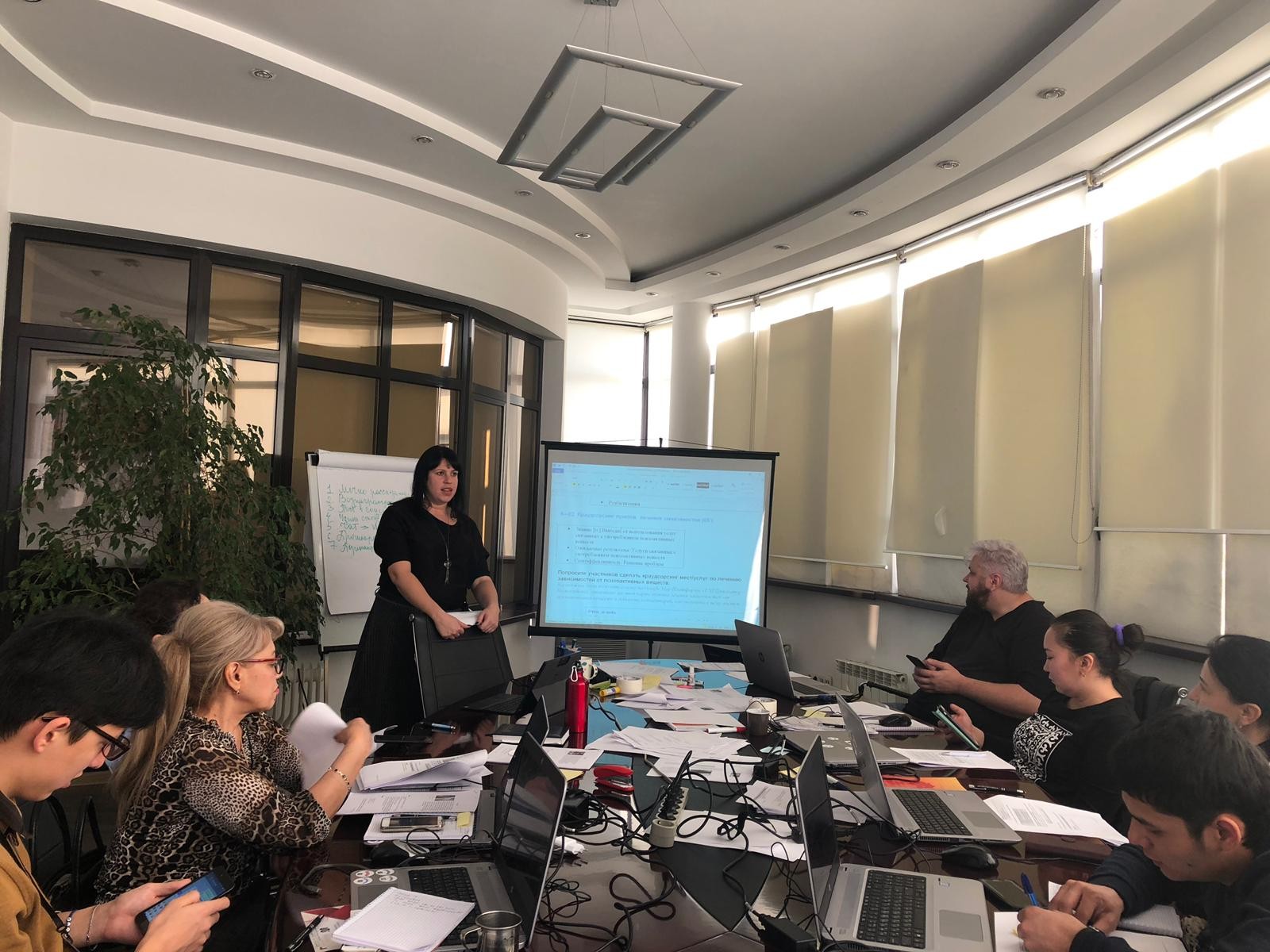 UNI staff roleplaying group program facilitation with UNI Research Assistant, Olga Balabekova Meeting around table, participants use phones