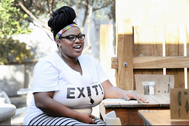 Grizelda Grootboom. Photo credit: African Independent Photo of Grizelda Grootboom laughing at a table outside with an Exit t-shirt
