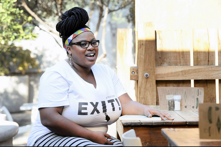 Photo of Grizelda Grootboom laughing at a table outside with an Exit t-shirt