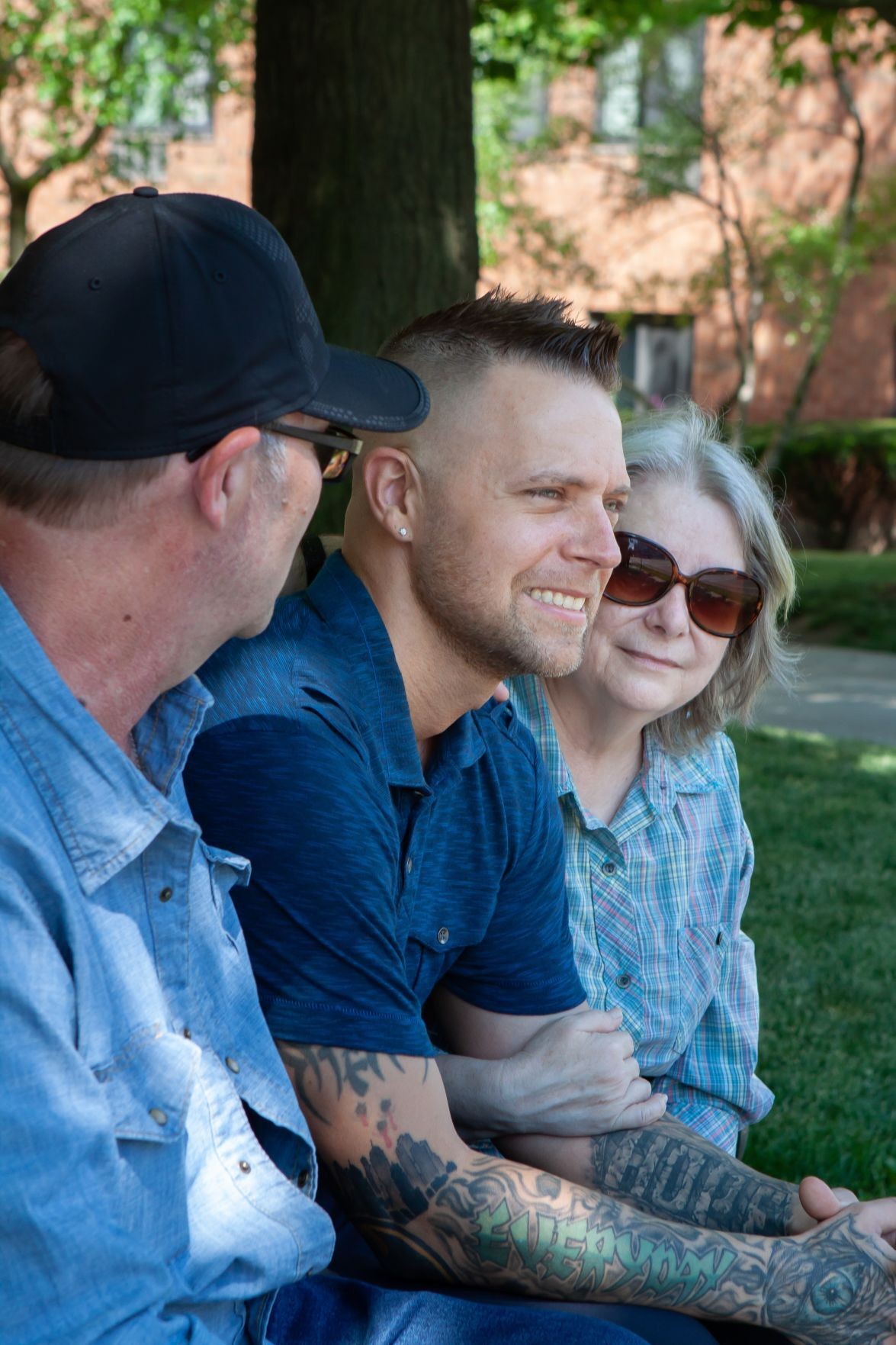 Bryan and two people hugging him sitting under a tree