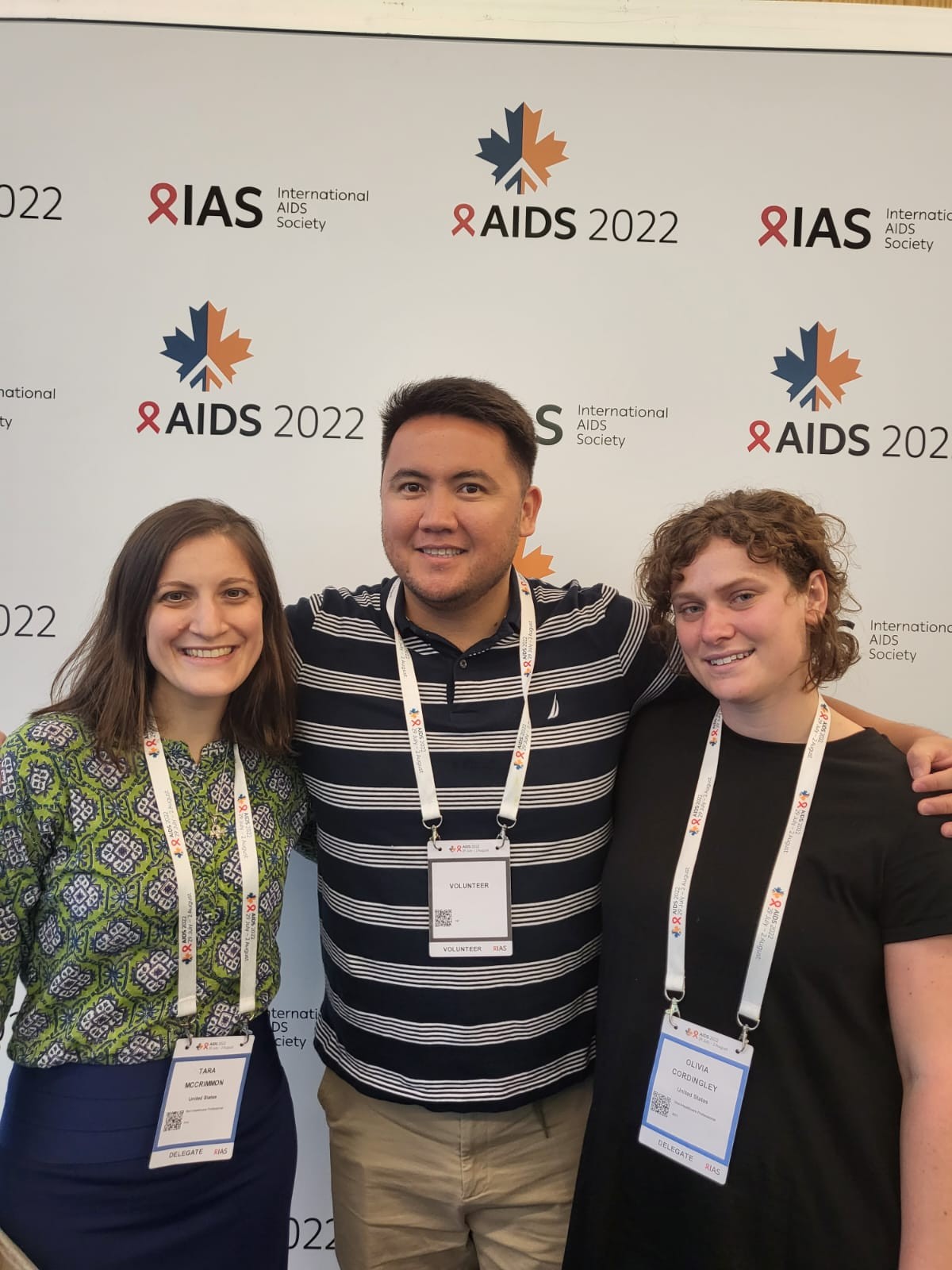 photo of Tara, Azamat, and Olivia in front of IAS logo at the conference