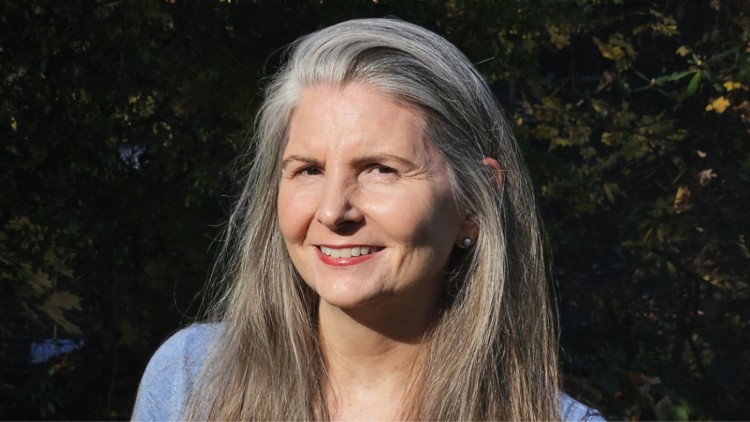 A woman with long gray hair smiles at the camera