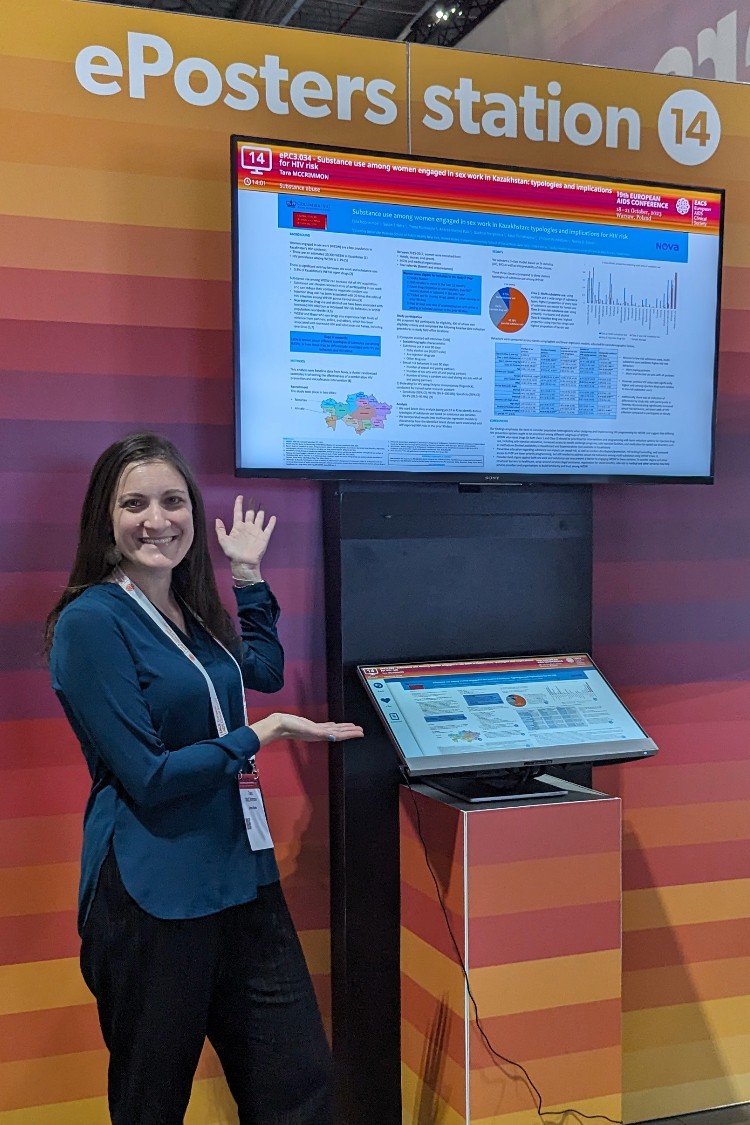 a woman in a blue shirt standing in front of a tv screen displaying a poster with graphs and text