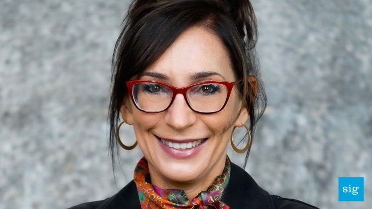 A woman with brown hair and red glasses smiles at the camera.