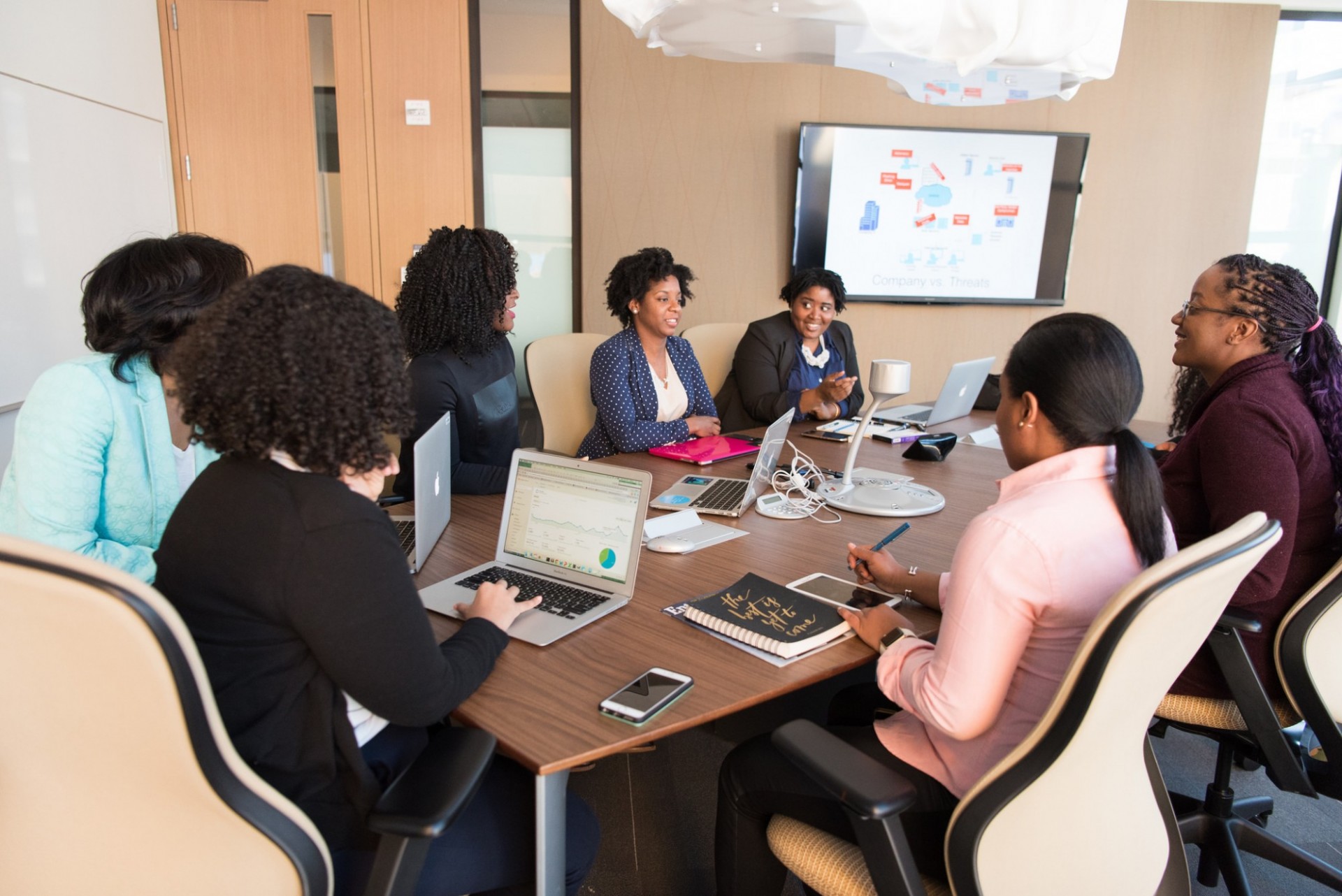Black women meeting at a board table and having a discussion with laptops