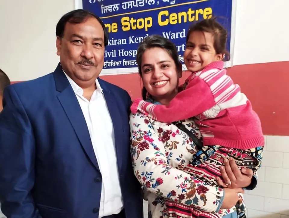 Two adults, the woman holding a child and smiling