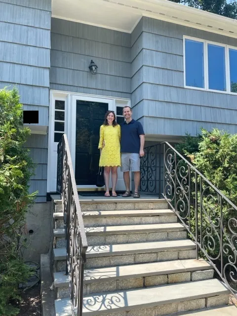 Jessica standing on top of stairs leading to the front door of her new blue-gray house