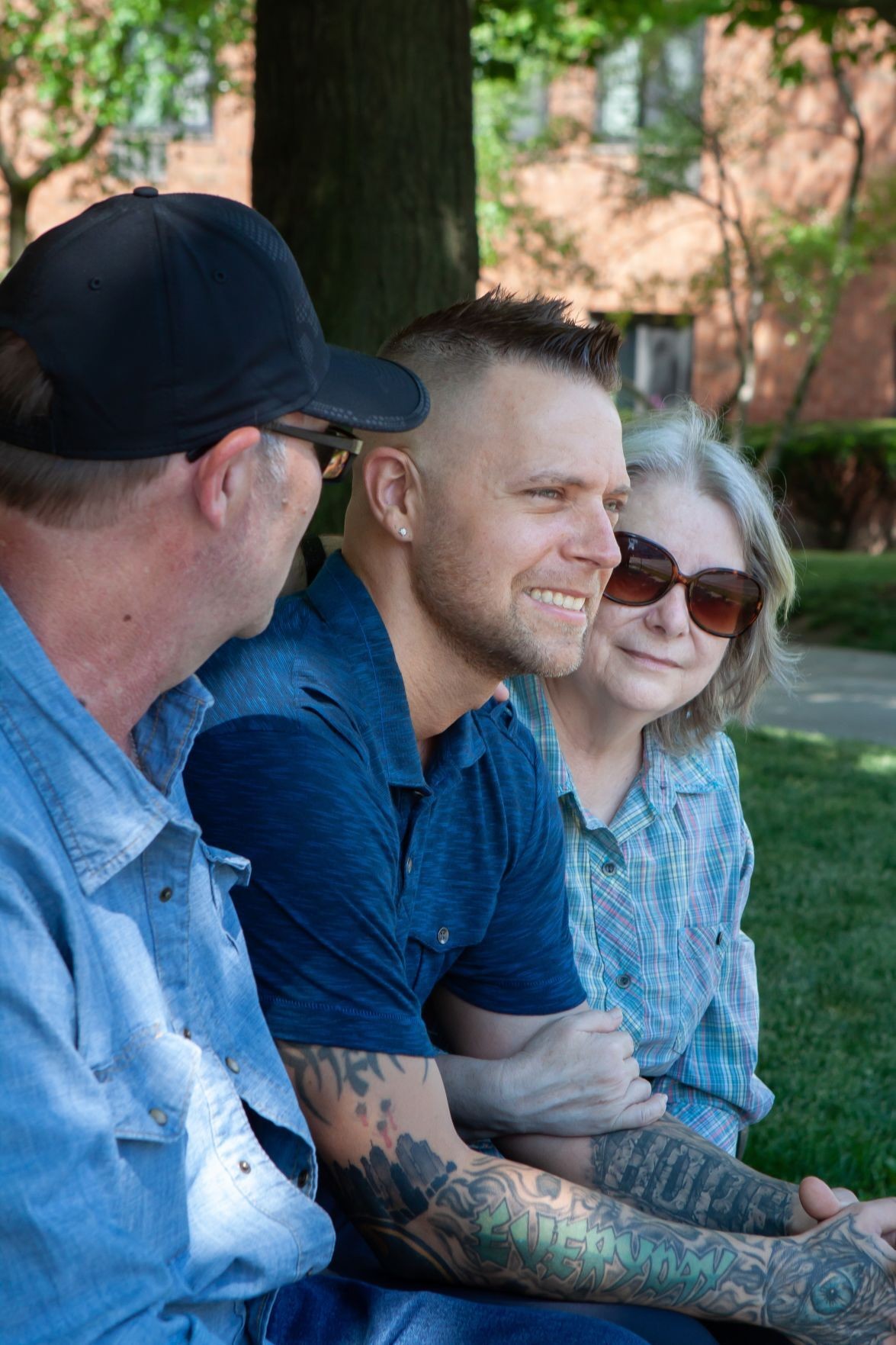 Photo of Bryan Bush by Devon Roblee, via The Auburn Pub Bryan and two people hugging him sitting under a tree