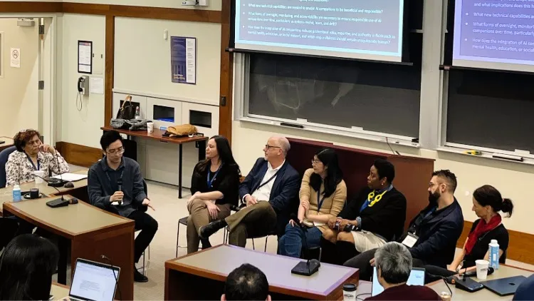 A panel of six people sit in front of display screens. There is also a moderator.
