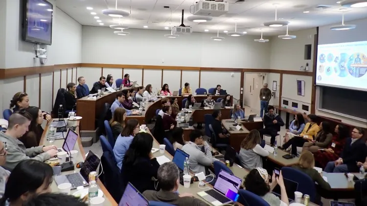A crowded room of people watching and taking notes on a presentation