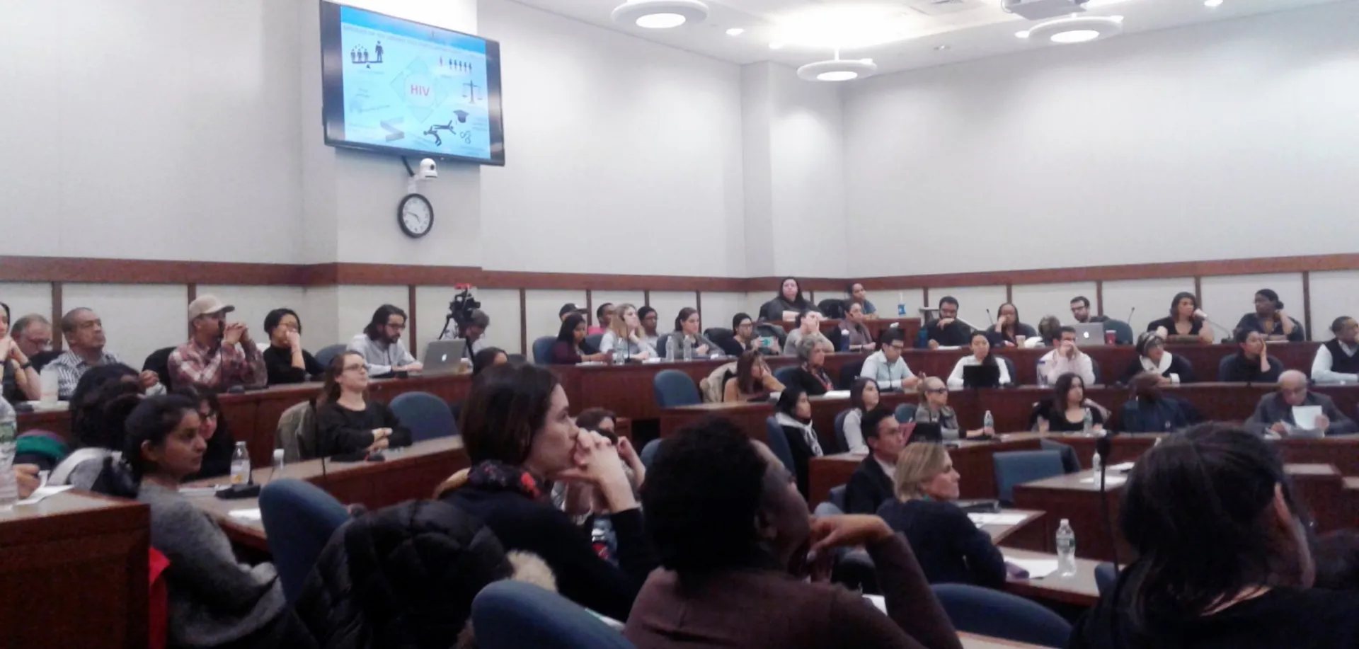 Audience for World AIDS Day event during Dr. Nabila El-Bassel's presentation, here showing the drivers of HIV on the back screen: stigma, discrimination, gender balance inequalities, and so many more forces that contribute to HIV.  