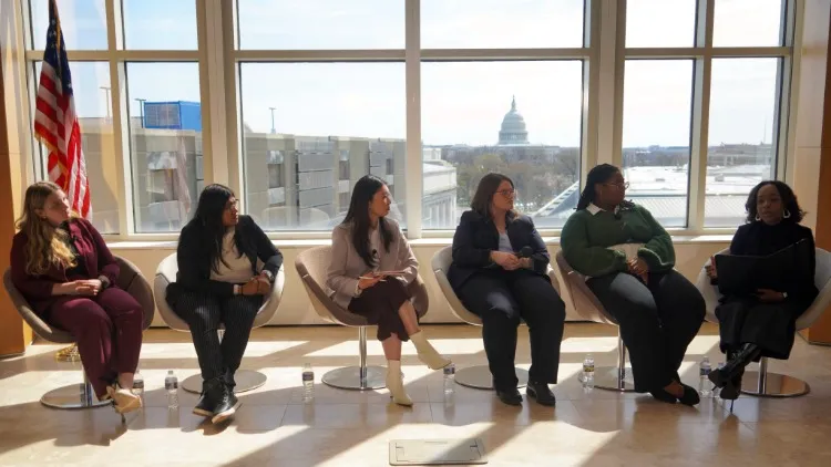Six MSW students in chairs in front of a large window through which the dome of the US Capitol Building is visible.