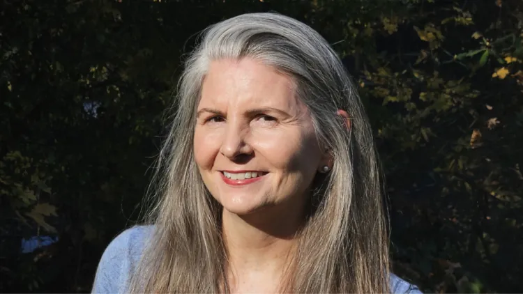 A woman with long gray hair smiles at the camera