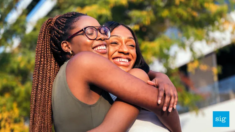 two women hugging. they're standing outside in the sunlight