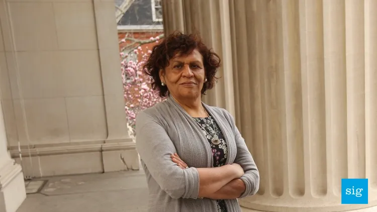 A woman in a gray cardigan standing in front of an ivory column