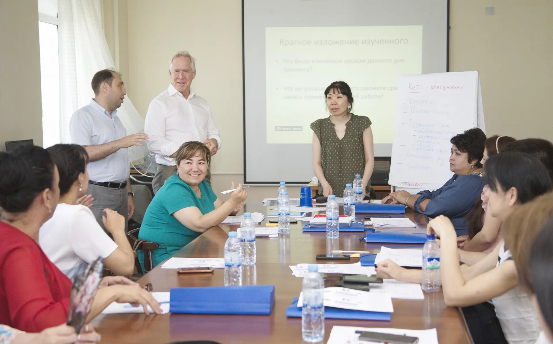 People sitting around a boardroom table being trained by L. Kim