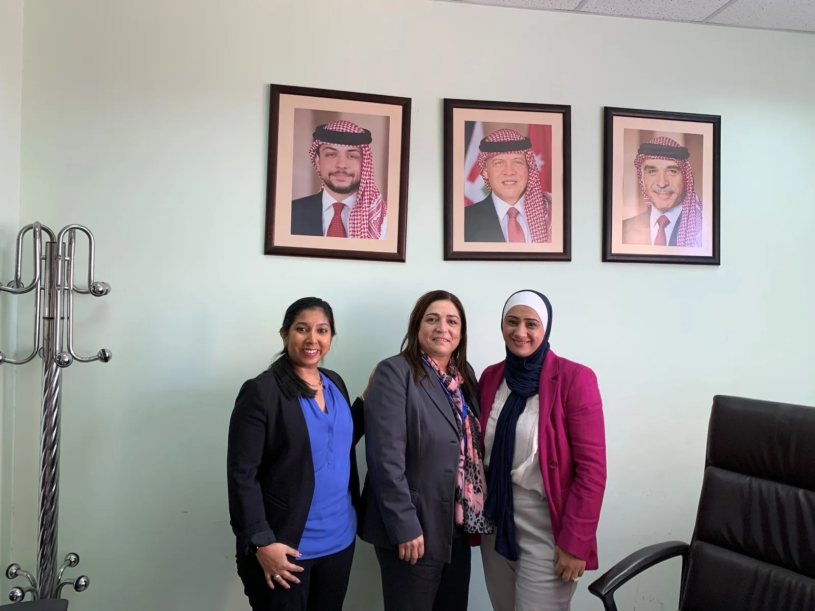 standing in front of photos of Jordanian leaders on the wall