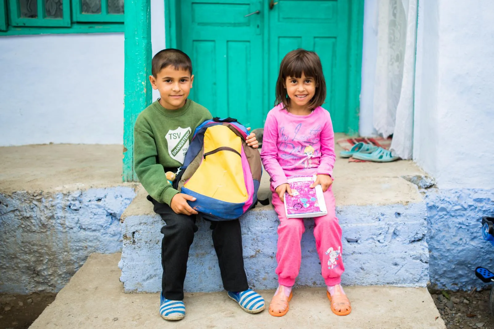 two children sitting in front of a colorful seafoam door