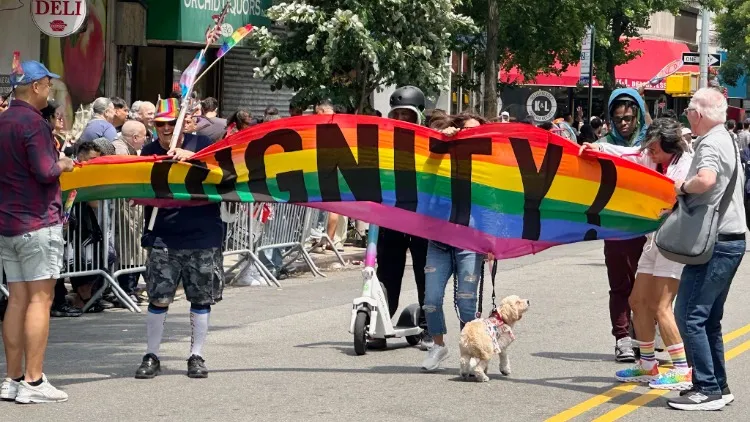 A rainbow banner with "dignity!" on it in large letters being carried through a street