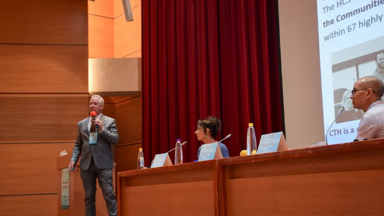 A man in a suit holds a microphone and speaks