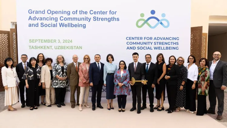 A large group of people standing in a row in front of a sign that says Grand Opening of the Center for Advancing Community Strengths and Social Wellbeing. One of them is holding a large golden key.