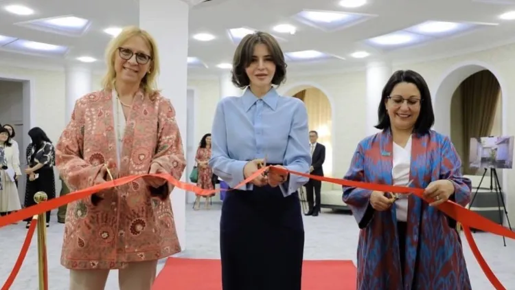 Three women holding scissors and cutting a red ribbon together.
